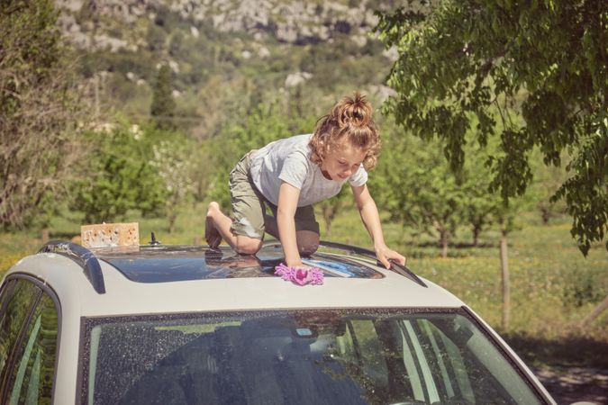 Focused kid with wash cloth and sponge on car roof in nature
