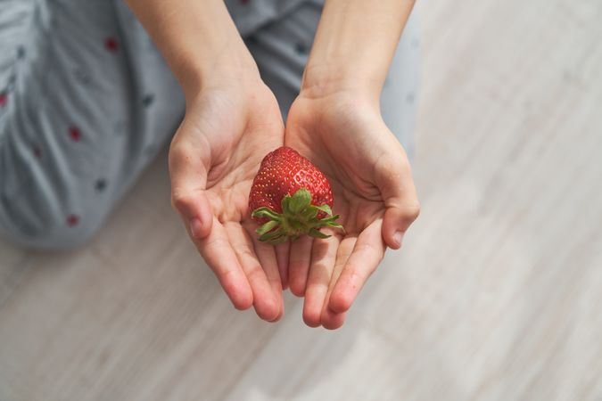 Anonymous person with cupped hands showing fresh strawberry