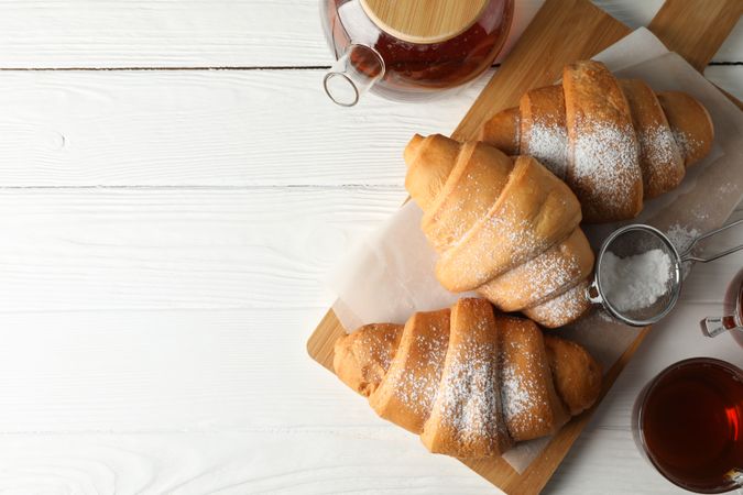 Looking down at tasty croissants and cups with tea on wooden cutting board, copy space