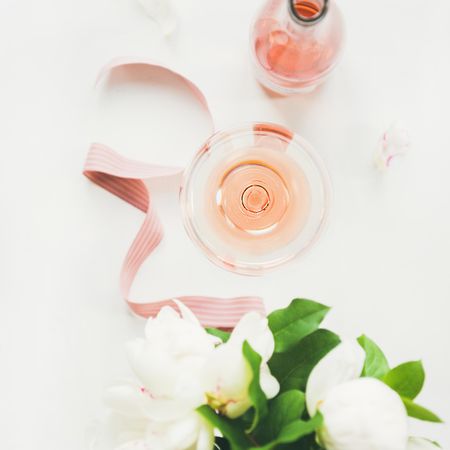 Top view of glass of pink rose wine, and bottle with flowers and ribbon, square crop