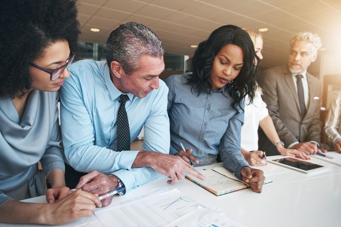 Group of colleagues in an office leaning over table going through notes