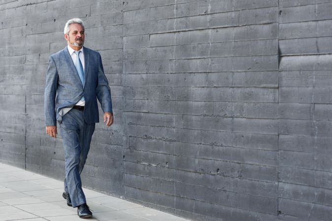 Successful business man wearing suit and walking next to concrete grey wall