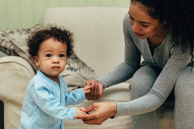 Woman holding toddler’s hands as he learns to walk