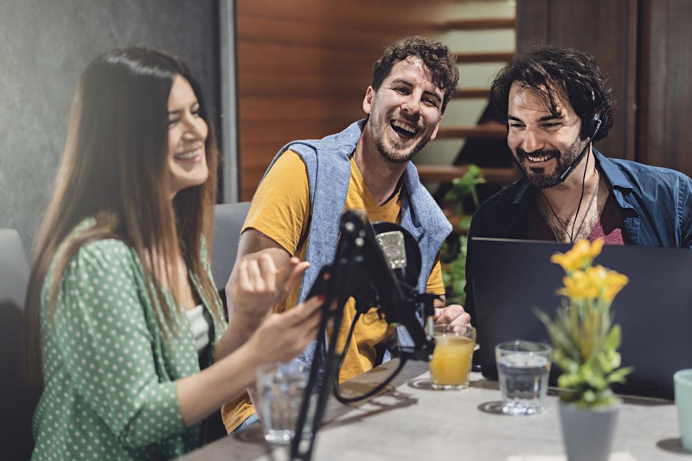 Group of young people recording a vlog video cast sitting around the table of their home studio