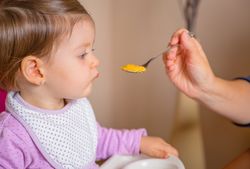 Baby eating puree from a spoon in the hand of mother