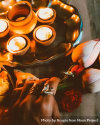 Cropped image of a hand holding a flower beside tray of lit diyas 5QMVg5
