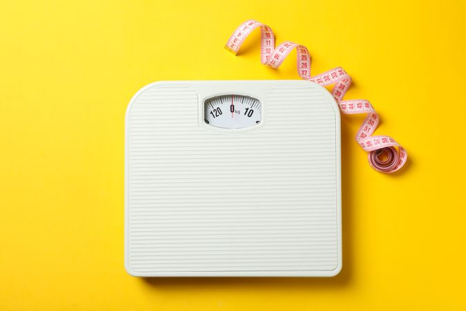 Scales and measuring tape on yellow background. Weight loss concept