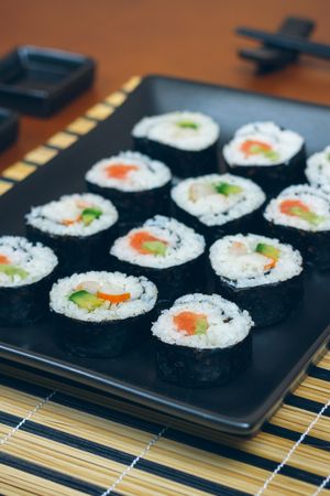 Freshly made sushi rolls on rectangular plate on mat