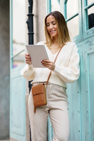 Happy woman in cream standing outside with digital tablet