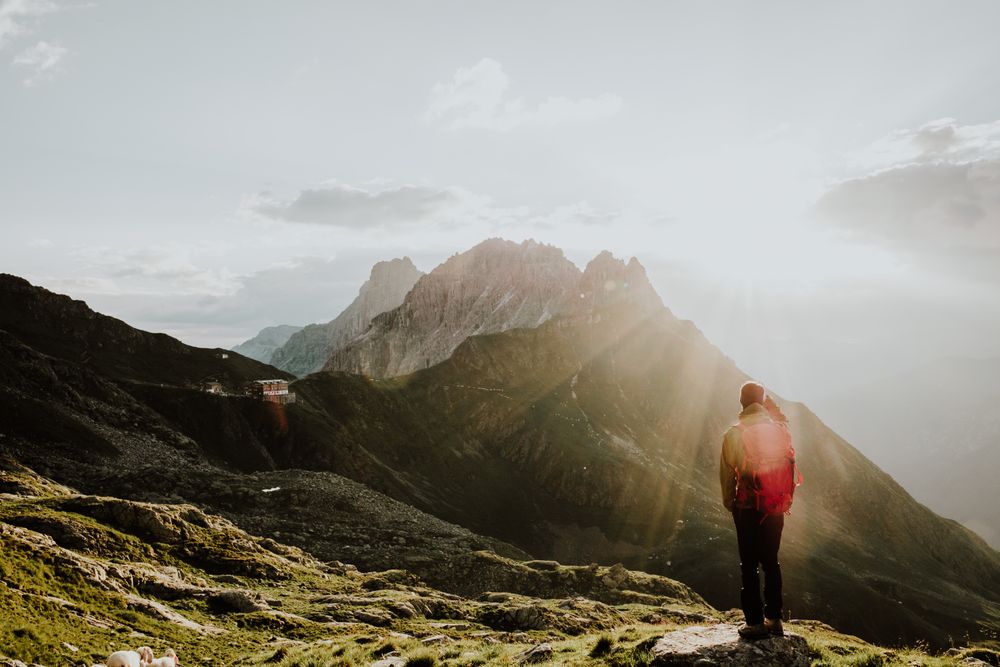 Man with backpack standing on rocky hill looking at mountains