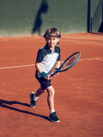 Adorable preteen boy playing tennis with racket on court