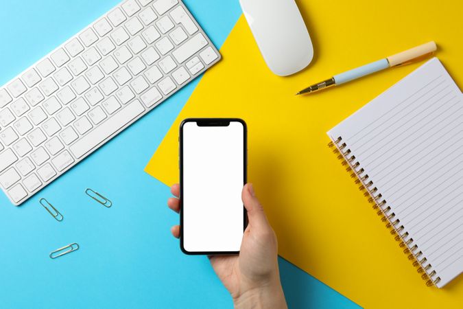 Female holding phone with empty screen. Workplace. Two - tone background
