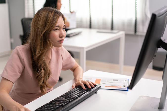 Asian woman squinting to see monitor in office