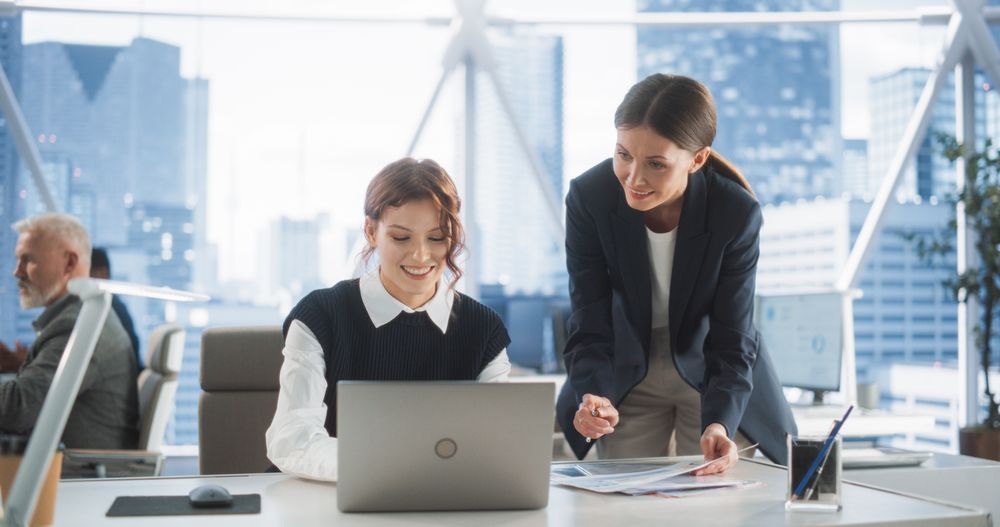 Professional Female Lawyer and Intern Talking And Working On Laptop Computer In Skyscraper Office In Downtown.
