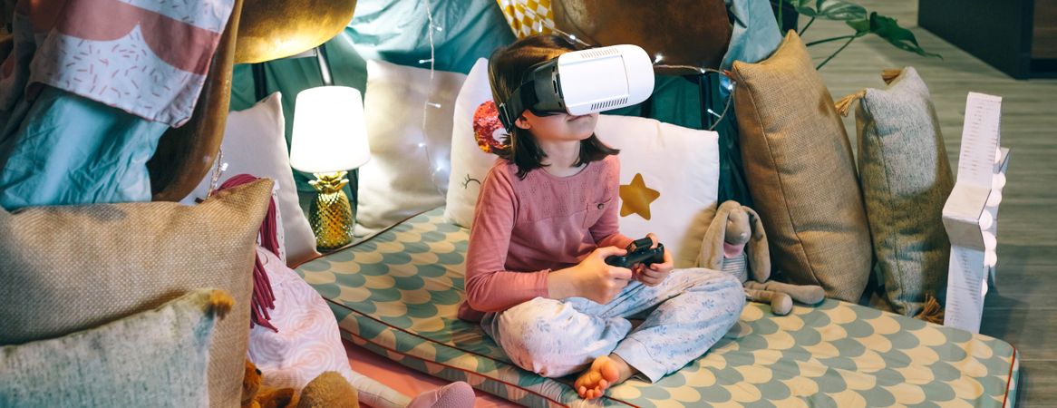 Banner of digital native child looking metaverse world through VR glasses sitting over mats in tent