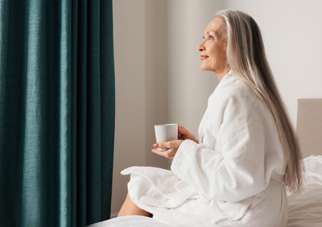 Older woman sitting on bed in bedroom and looking away
