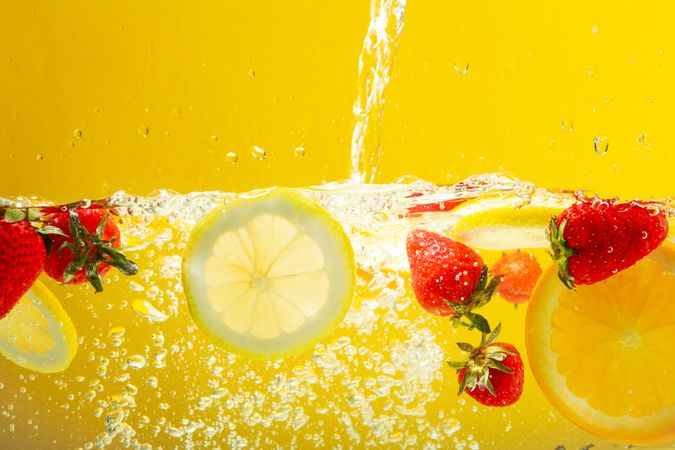 Citrus slices and strawberries floating in water in yellow background