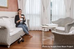 Woman in blazer drinking coffee and sitting on couch beMdqb