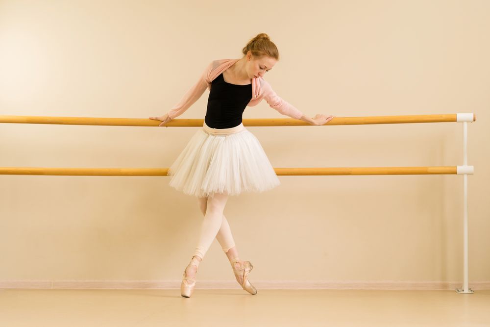 Poised ballerina stands on pointe while lightly holding barre
