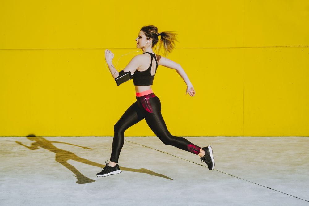 Woman with earphones running near wall