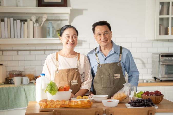 Portrait of Asian mature couple in apron cooking in the kitchen together and looking at camera