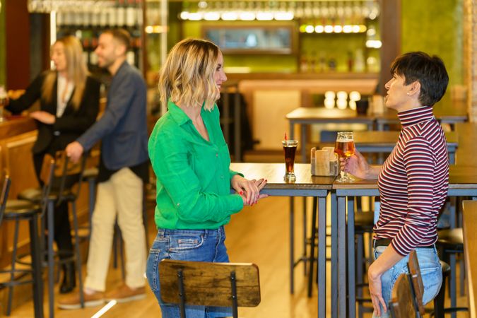 Female friends standing at bar table with drinks