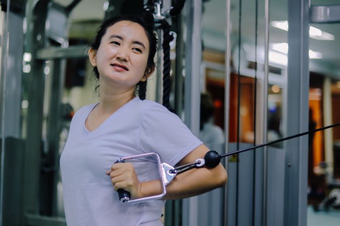A woman with a focused expression is in a fitness center, using a cable machine to exercise.