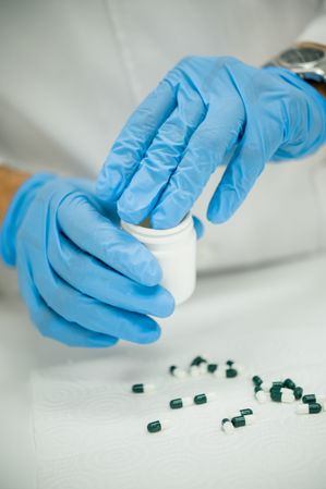 Crop pharmacist in gloves putting capsules into bottle