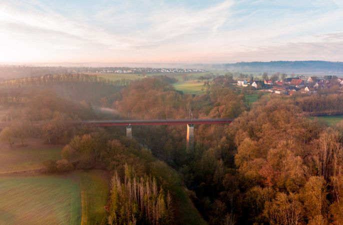 Railway bridge crossing river surrounded by nature, drone shot at sunrise