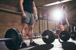 Crop shot of male standing beside barbell with weights