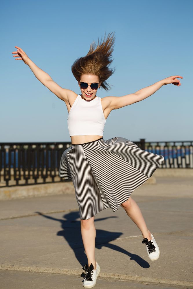 Smiling female in striped skirt joyously jumping near water