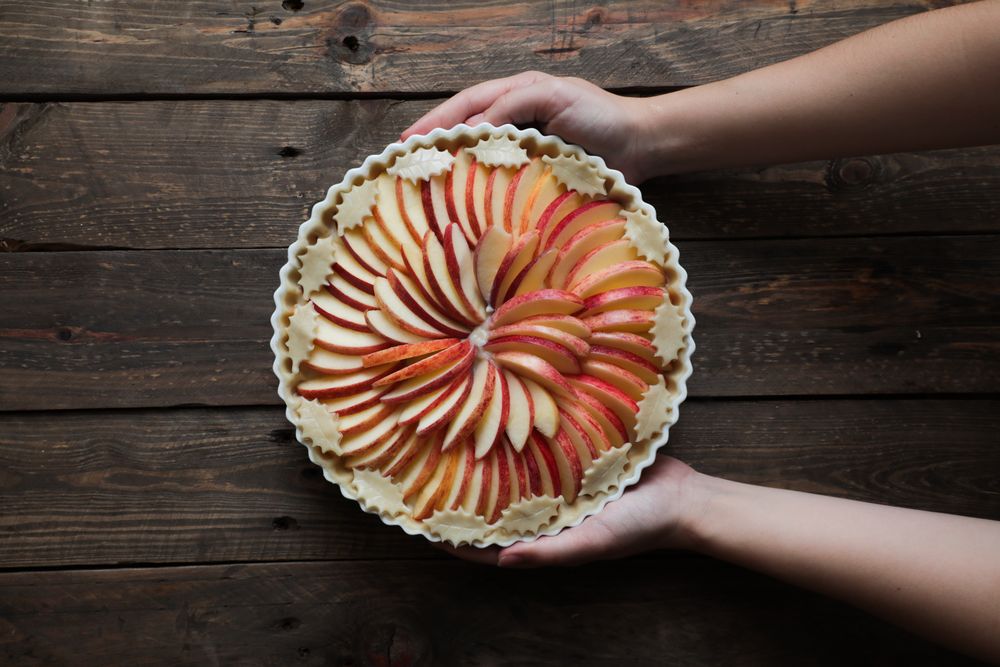 unrecognizable woman showing a tasty apple pie on a wooden table