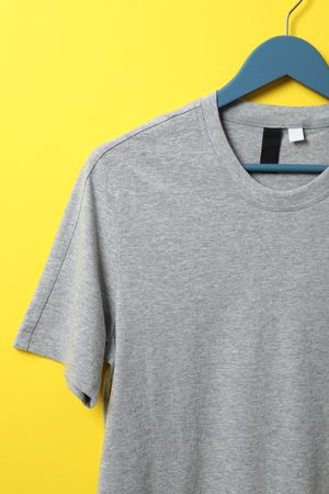 Hanger with blank gray t-shirt on yellow background, space for text
