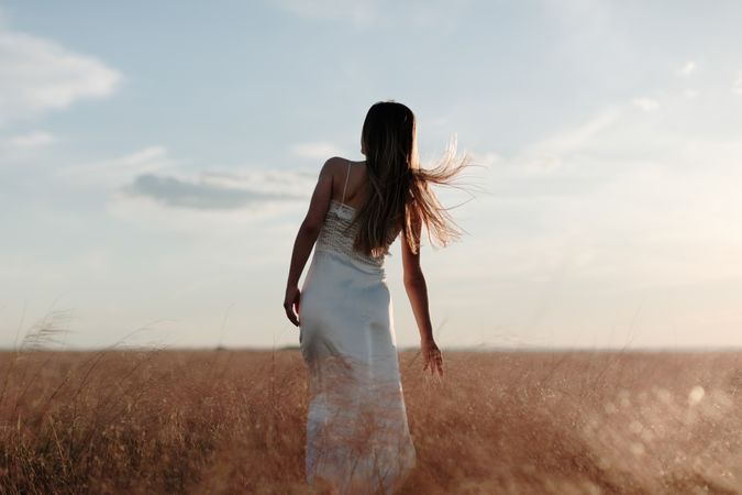 Back view of young woman in a dress standing in an open field