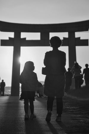 Back view of mother and child standing near Torii in grayscale