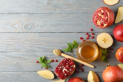 Top view of honey pot surrounded by slices apples and pomegranate on grey table with copy space