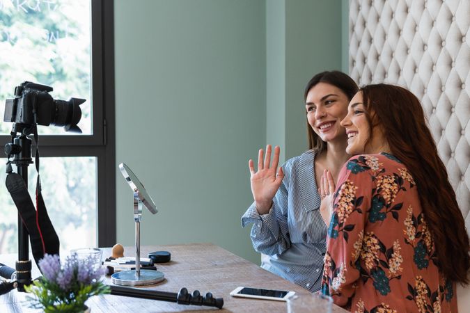 Cheerful young women recording video while sitting at table