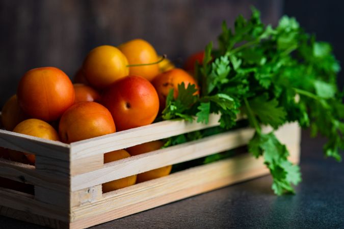 Wooden box of plums with parsley