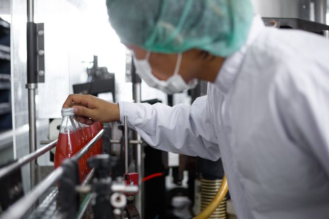 Asian man worker inspecting drink product on bottling factory machinery.