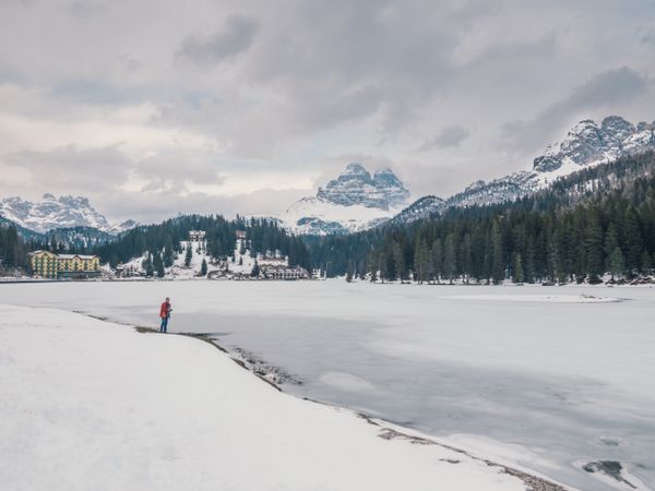 Unrecognizable person standing in snow surrounded by forest and mountains