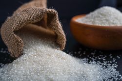 sugar spilling from a burlap sack beside a full bowl