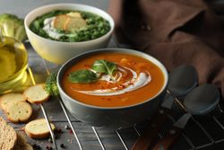 Two bowls of orange and green soup on wooden table with crackers