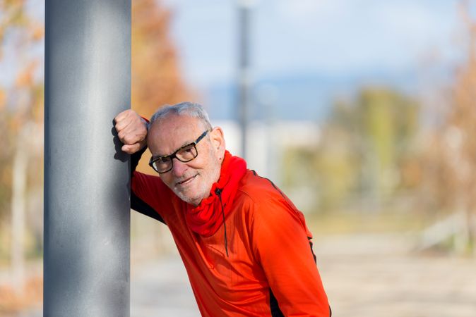 Smiling older male leaning on pole in park
