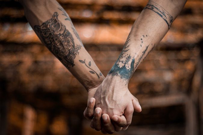 Cropped image of two people with tattooed sleeve holding hands