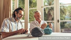 Older men sitting at home and knitting sweater with the knitting needles and woolen threads 4OrdZ5
