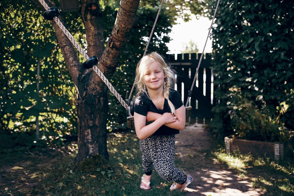Smiling blonde girl with braided hair sitting on outdoor swing