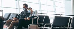 Man and woman with face masks sitting at airport terminal waiting lounge bGmaA5