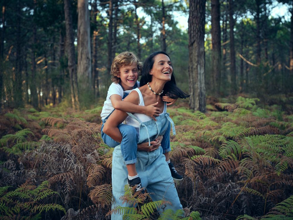 Son riding back of mother during walk in woods