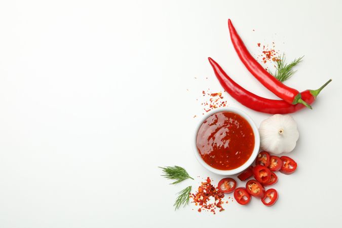 Bowl with chilli sauce, pepper and garlic on blank background