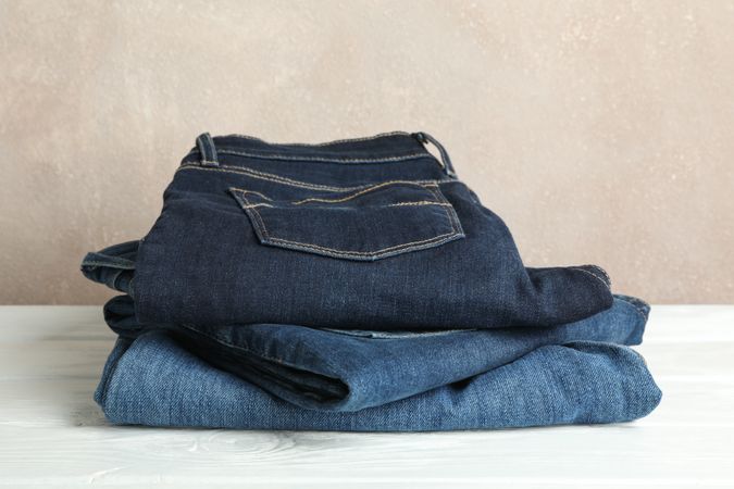 Stack of jeans pants on light background, space for text